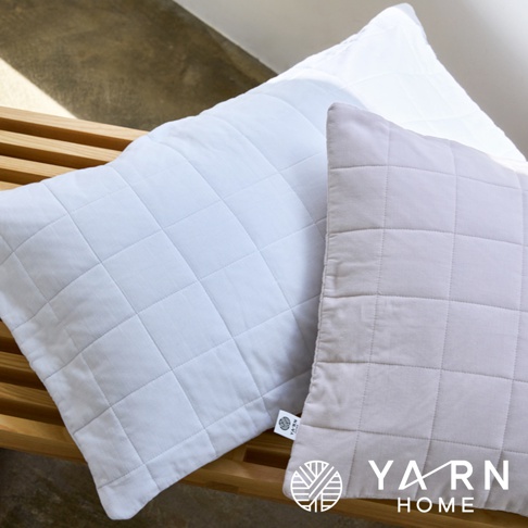 兩件格紋枕套，一件為淺藍色，一件為淺灰色，皆為脫脂棉混紗材質，表面有菱格紋縫線，置於木製長凳上。