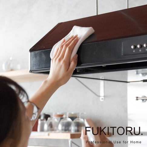 一隻手拿著白色超細纖維擦拭布，正在擦拭黑色抽油煙機的頂部。