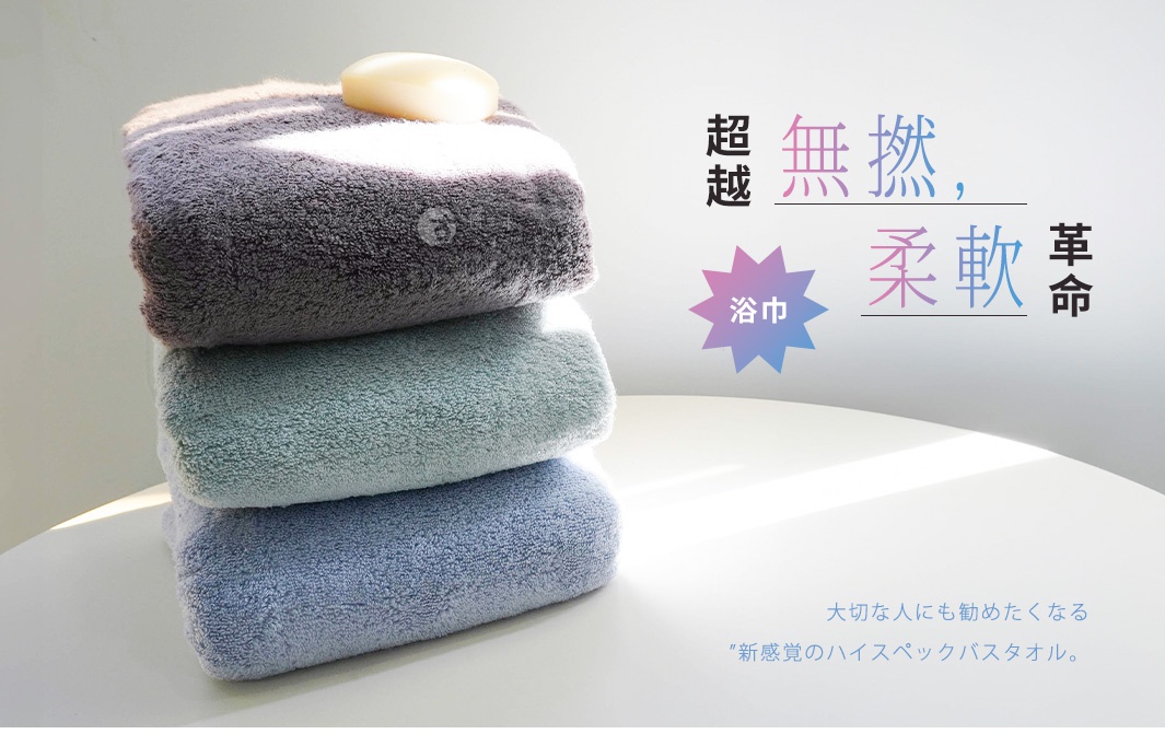 堆疊的浴巾，上面放著一塊香皂，搭配日文廣告詞「超越 無撚 柔軟 革命」、「浴巾」及「送給重要的人」、「新感覺的高規格浴巾」。