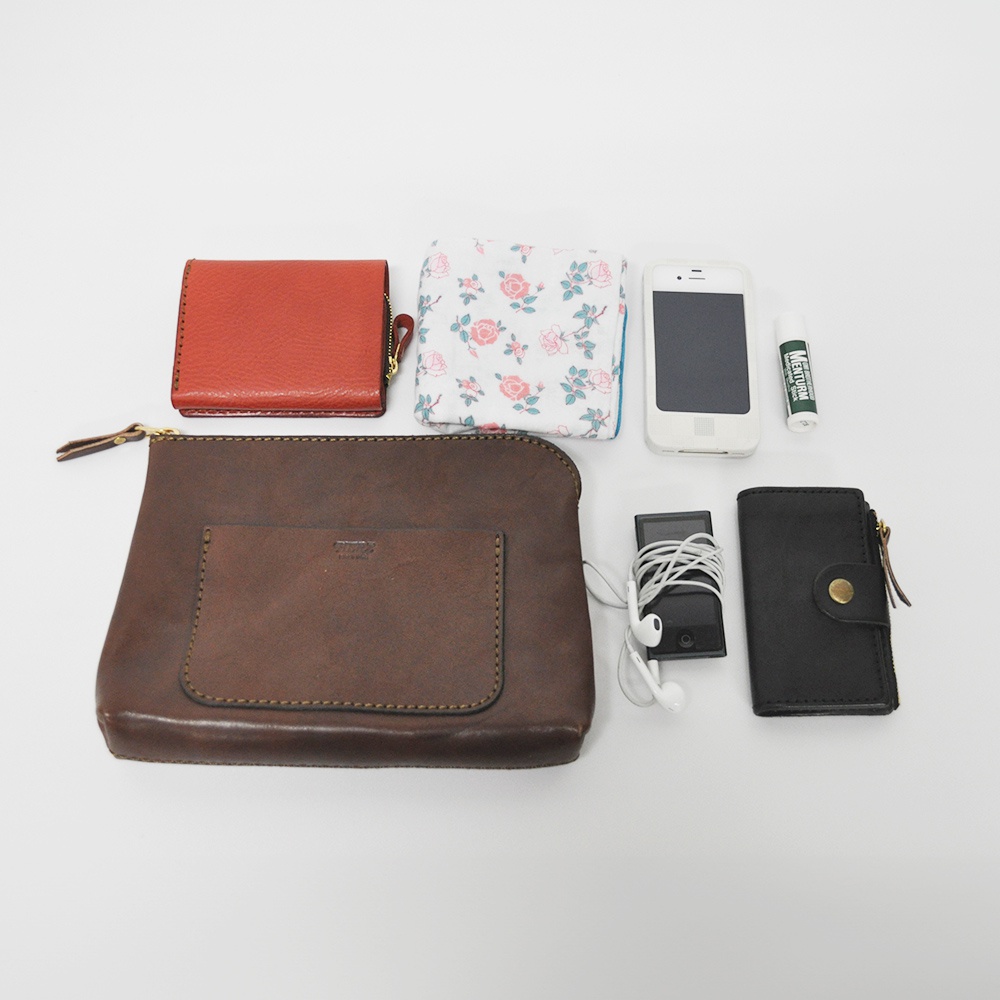 職人手作皮革小物收納包 KF-114 L，展示紅、棕、黑三色皮革小物，包含一個紅色皮夾、一個深棕色皮革收納包、一個黑色皮夾，以及其他配件如手機、耳機、護唇膏和花卉圖案布巾。