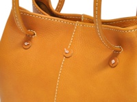 職人手作皮革兩用托特包，呈現溫暖的橘褐色，質樸的皮革紋理搭配米白色縫線，展現細膩工藝。包款設有兩個可調式束口設計，簡潔實用。