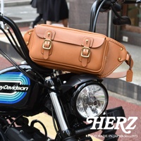 職人手作皮革騎士隨身斜背包，採用淺棕色皮革，設有兩個金色釦環及側邊金色铆釘，設計簡約實用，適合搭配機車。