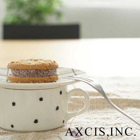 白色美濃燒手繪馬克杯，點綴黑色圓點，杯蓋上放著夾心餅乾，旁有一支叉子。