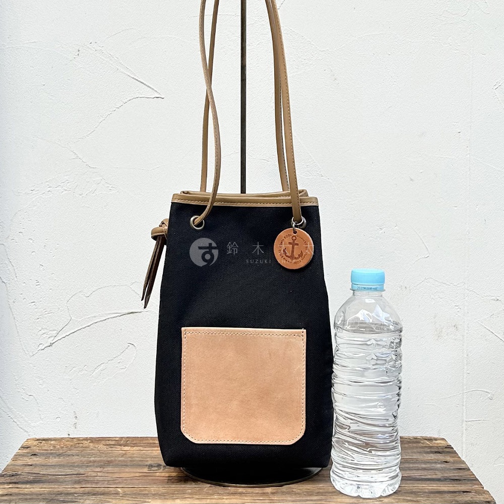 神戶clueto 黑色防潑水尼龍束口肩背包，配有義大利皮革前袋及船錨吊飾，旁為一瓶水。