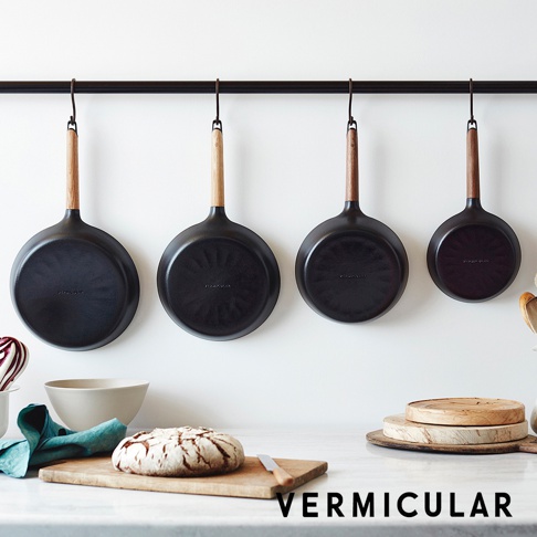 日本製黑色琺瑯鑄鐵平底深鍋，附木質手柄，掛於廚房掛桿上，鍋底品牌標誌清晰可見。