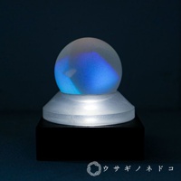 霧面質感的透明稜鏡球，內部呈現藍色漸層光影，置於透明的圓形底座上，再搭配底部黑色方形底座。