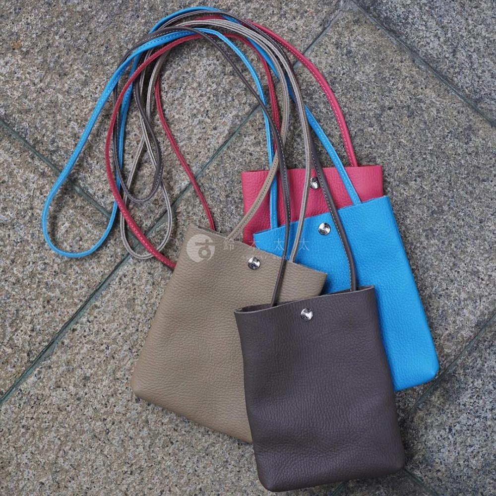 三款京都職人手作隨身手機包，分別為大地色、桃紅色及亮藍色，皆為柔軟皮革材質，搭配細長同色系背帶，設計簡約時尚。