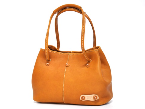 焦糖色皮革兩用托特包，包身線條圓潤，以米白色車線縫製，提把設計簡潔，底部右側有品牌皮革標籤。