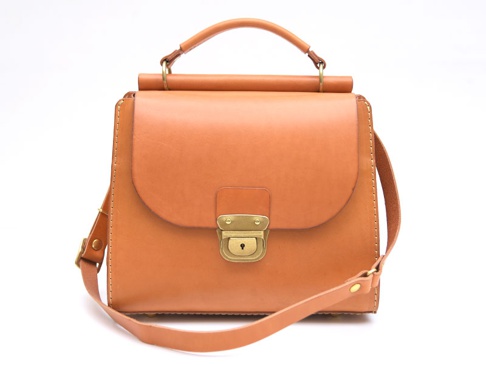 職人手作屋瓦風兩用單肩包，以淺棕色皮革製成，包款設計簡約，配有金色鎖扣及提把，可手提或斜肩背。