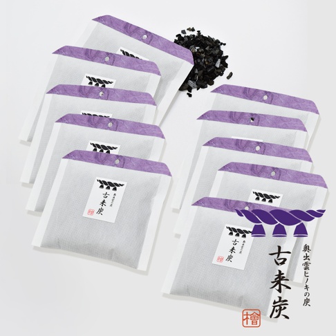 一堆古來炭迷你調濕木炭包，每包皆為淺灰色網狀材質，頂部有紫色紙質邊緣，中心印有黑色圖案和中文標籤。旁邊散落著黑色炭粒。