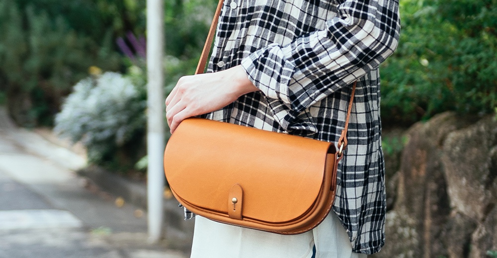 職人手作皮革迷你馬鞍包，顏色為焦糖棕，以天然皮革製成，設計簡約，帶有翻蓋與金屬釦設計。