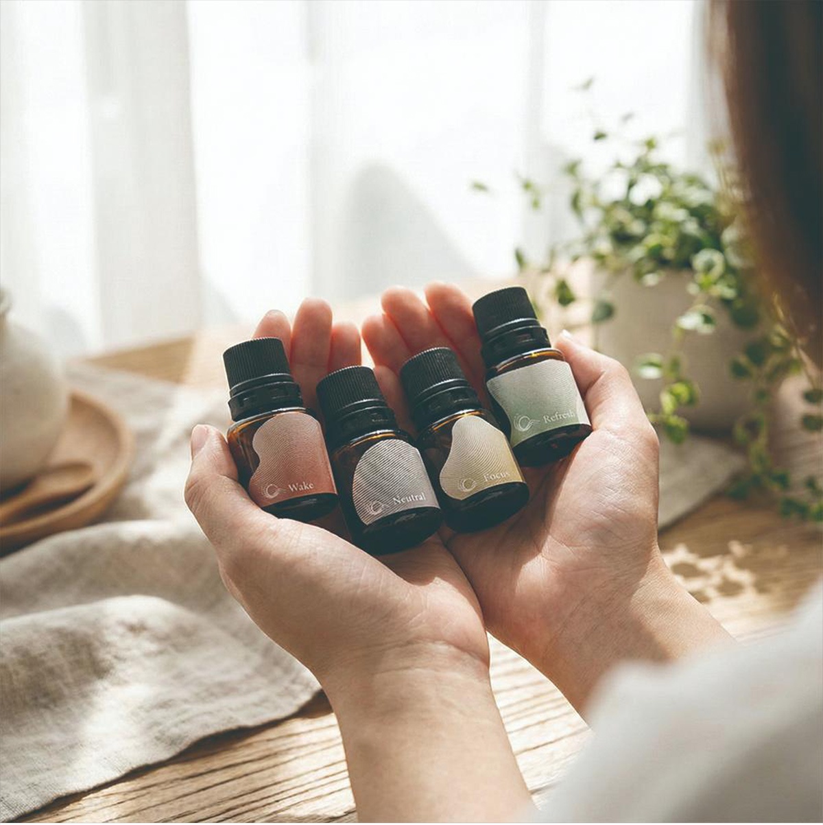 一雙手捧著四瓶精油，瓶身上分別標有「Wake」、「Neutral」、「Focus」和「Refresh」的字樣。