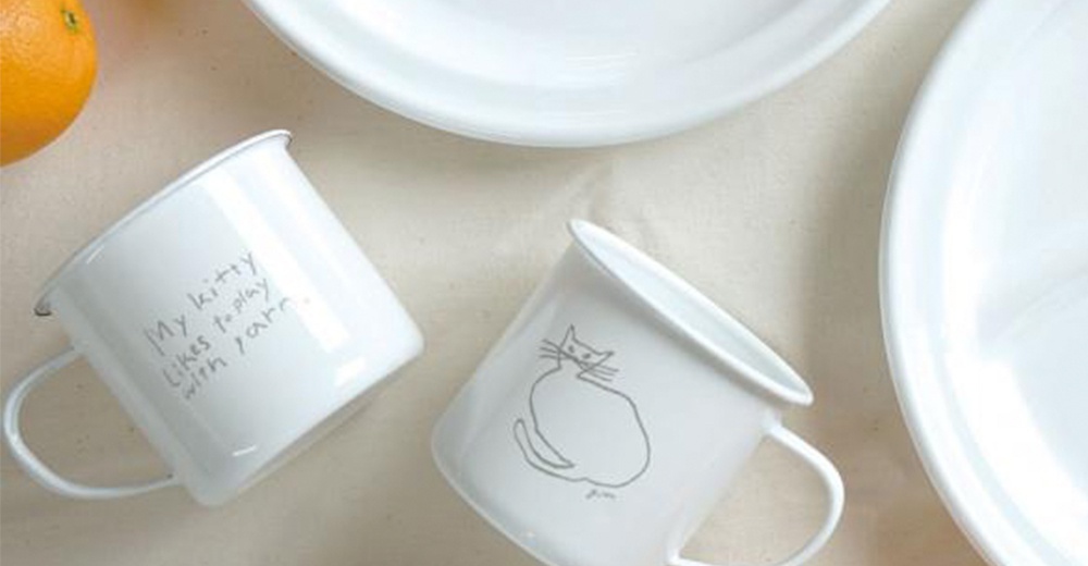 兩個白色琺瑯馬克杯，其中一個印有貓咪圖案，另一側印有英文文字「My kitty likes to play with yarn」。