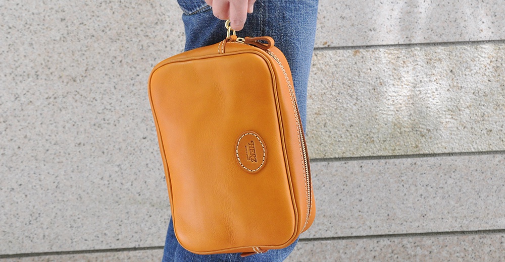 職人手作皮革可拆式扣環萬用手提包，棕褐色皮革材質，配有拉鍊開合和一個橢圓形品牌標誌。