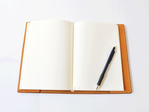 棕色皮革製成的 B5 筆記本書套，內含兩頁空白筆記本內頁，一支藍色原子筆橫放在右側內頁上。