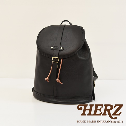 黑色皮革單扣束口後背包，配有金屬釦帶和綁繩，包身線條簡潔，適合日常使用。