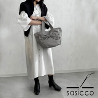 三河木綿刺子織材質的灰色托特包，包身前方有大蝴蝶結裝飾，搭配白色長洋裝與黑色靴子。