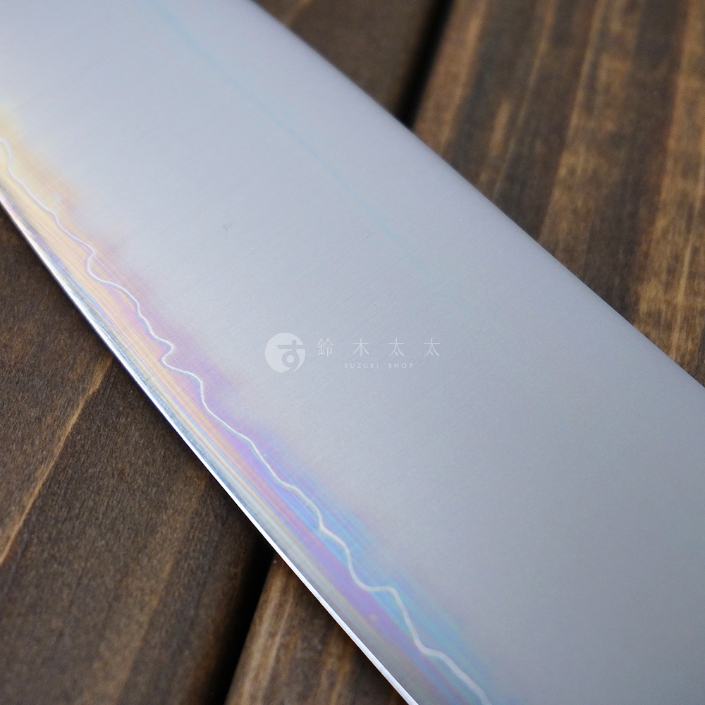 [景清] Chromax鋼三德刀-(胡桃木18cm)，刀身為銀色Chromax鋼，帶有彩虹色澤的波浪狀花紋，刀刃鋒利，置於深棕色木紋背景上。