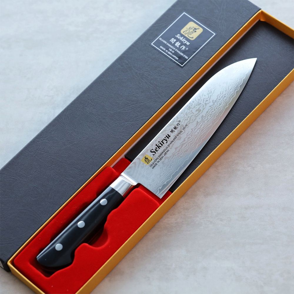 VG10不鏽鋼33層大馬士革三德刀，刀刃呈現獨特波浪紋路，搭配黑色握柄，置於紅色襯墊的黑色禮盒中。