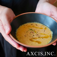 雙手捧著一個素燒陶瓷沙拉碗，碗內盛有濃湯，表面撒有黑胡椒和香草碎。碗外緣為陶土原色，碗內為黑色，呈現簡約設計。