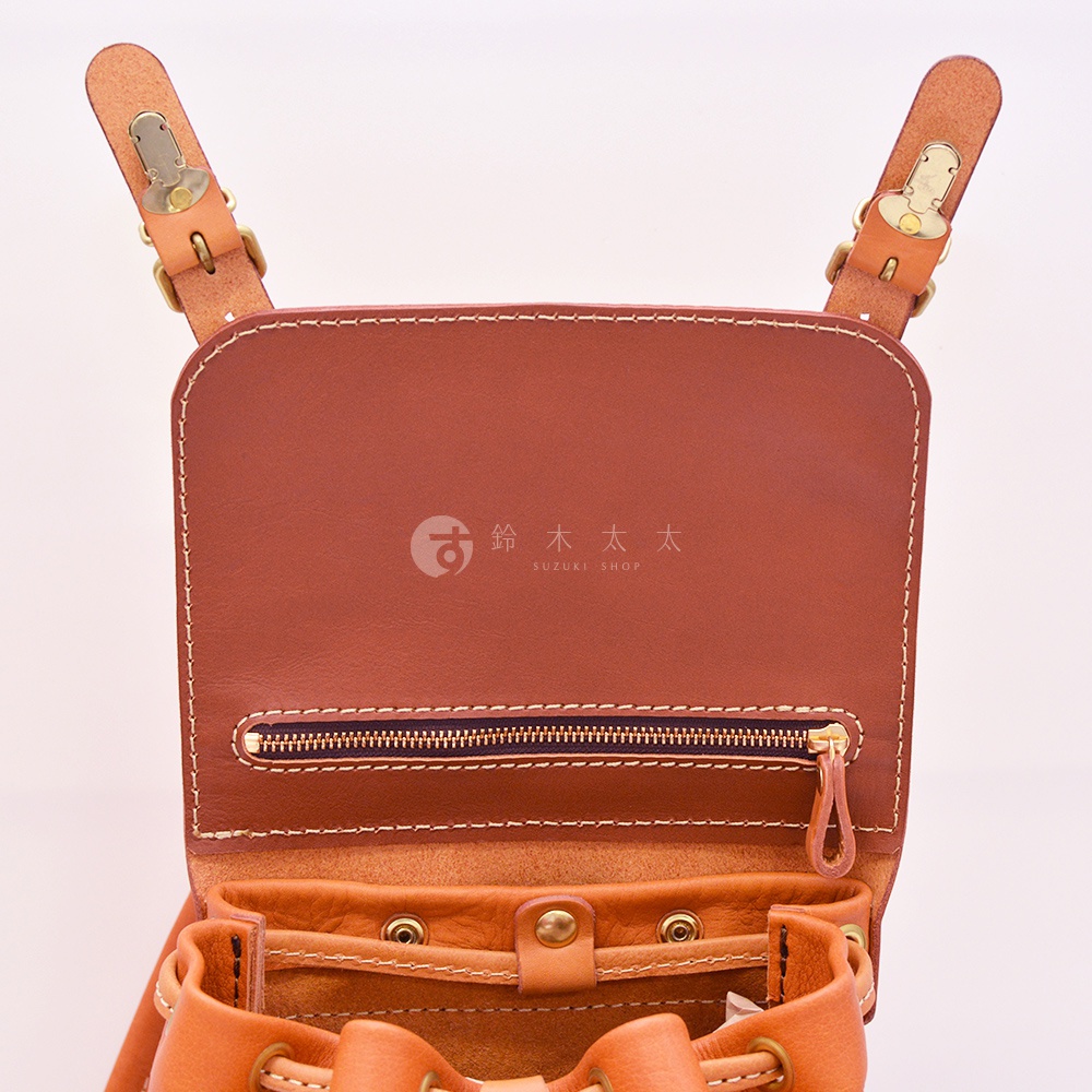 棕色皮革復古風旅行後背包，頂部翻蓋設計，帶有金色金屬扣環，中央有拉鍊開口，下方是抽繩束口設計，整體以精緻縫線裝飾。