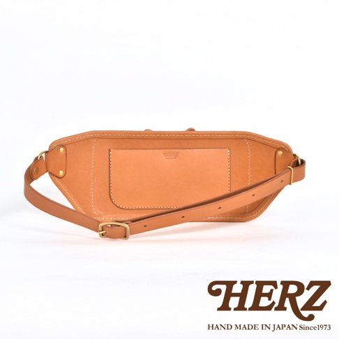 簡潔的駝色皮革騎士斜背包，設有外置口袋和可調節式肩帶，以細緻的縫線和金屬扣件裝飾。