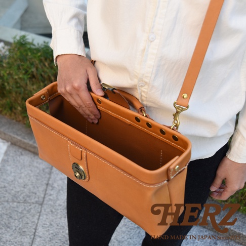 HERZ 職人手作皮革橫長形杜勒斯單肩包，棕褐色皮革材質，配有可調節肩背帶，包款經典簡約，男女皆適用。
