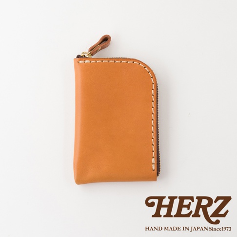 日本HERZ職人手作皮革分隔收納迷你錢包，選用棕色Stare皮革製作，外觀簡約並採L型拉鍊設計，側面綴有精緻縫線細節，下方印有品牌名稱與創始年份標誌。