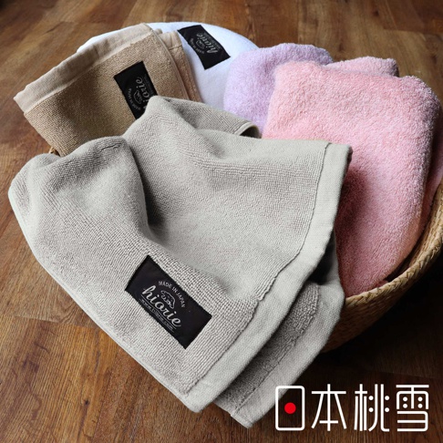 籃子裡擺放著多條質地柔軟的毛巾，顏色包括淺灰色、米色、淡紫色和粉紅色。其中淺灰色毛巾靠近畫面，上面有黑色標籤，印有「hiarie」字樣及「MADE IN JAPAN」字樣。