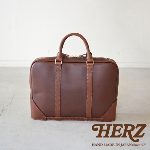職人手作皮革Organ商務公事包，深棕色皮革，帶有兩條皮革提把及拉鍊開口，底部有加強皮革裝飾，整體呈現復古質感。