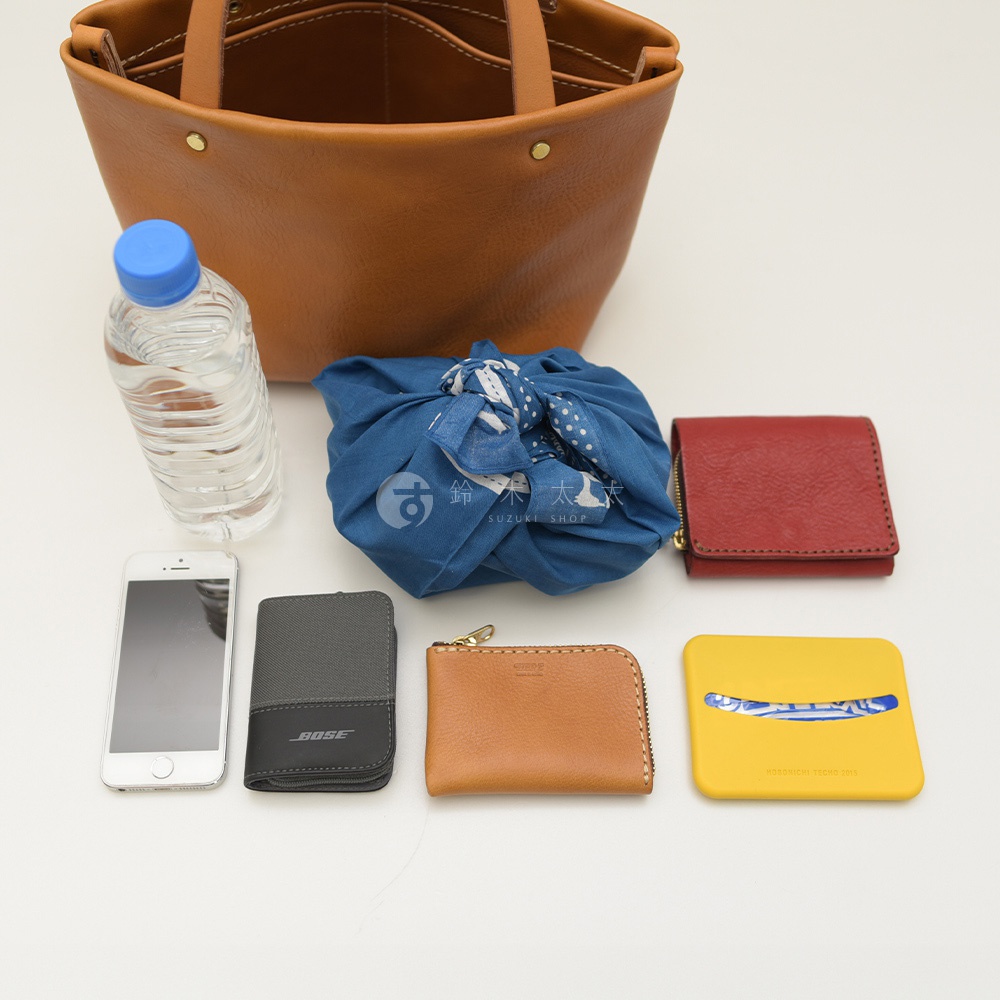咖啡色皮革托特包，內有四個隔層，旁邊擺放一瓶礦泉水、藍色印花布包、紅色皮夾、灰色名片夾、棕色零錢包及黃色杯墊。