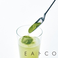 銀色金屬製的小長勺，正將綠色粉末舀入裝有淺綠色飲品的透明玻璃杯中。