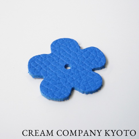 藍色皮革製成的五瓣花形吊飾，表面有壓紋，中央有一個小圓孔，適合用於隨身手機包。