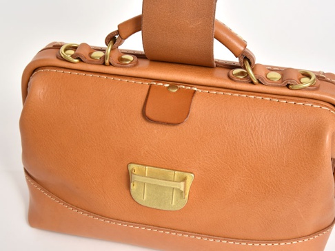 咖啡色皮革製成的兩用迷你口金包，綴有黃銅色金屬扣環和飾件，搭配皮革提把和縫線細節，展現職人手作質感。