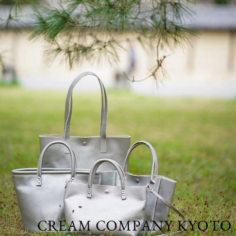 四個銀色皮革隨身手機包，其中一個較大的托特包，三個較小的手提包，搭配綠色草地和樹枝背景。