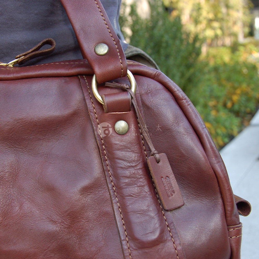 深棕色水洗皮革迷你波士頓包，側面特寫，展示了包包的皮革紋理、縫線細節、金屬扣件及吊牌。
