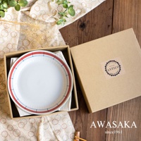 一組五個白色陶瓷盤，盤緣飾有紅色與藍色線條，置於紙盒內，旁邊為一個牛皮紙盒，盒上貼有「VINTAGE STYLE ANTICO MADE IN JAPAN」標籤，背景為木紋桌面與印有圓圈圖案的布料。