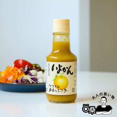 一瓶150毫升的無油柑橘風味沙拉醬，醬汁呈黃綠色，瓶身有日文標籤，印有柑橘圖案。背景為一盤色彩豐富的沙拉。