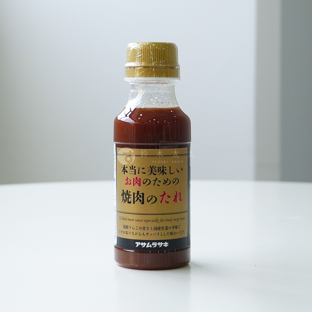 一瓶金蓋透明塑膠瓶身的朝紫燒肉醬，瓶標中央以大字標示真的很好吃的肉料理調味醬，上方印有鈴木商店標誌，下方則以小字說明採用國產蘋果與生薑調味，整體呈現深褐色醬汁質感。