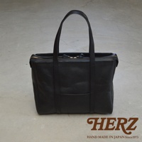 黑色皮革手提包，方形設計，頂部拉鍊開合，設有雙提把，包身正面有一個貼袋，材質為粒面皮革。