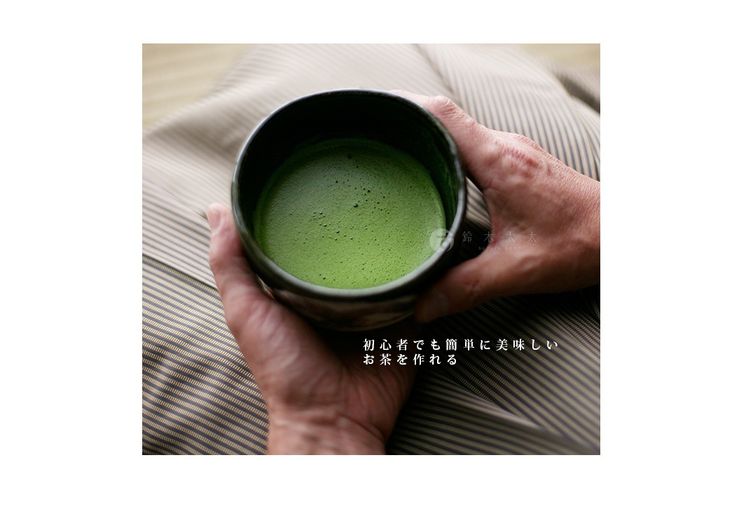 雙手捧著裝有翠綠抹茶的黑色茶碗，茶碗放置在條紋布料上。