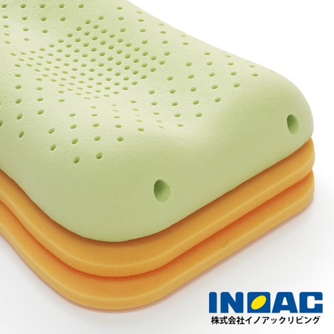 淺綠色記憶棉枕頭堆疊在兩層橘色海綿墊上，枕頭表面佈滿圓形透氣孔，呈現波浪狀凹槽設計。