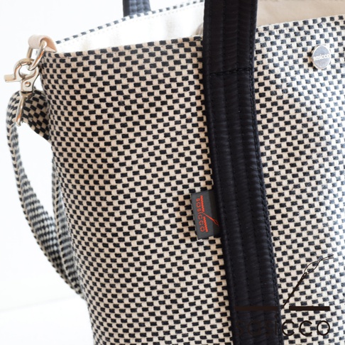 三河木綿刺子織兩用水桶包，黑白格紋織紋，配有黑色織帶提把、可拆卸肩帶及品牌標籤。