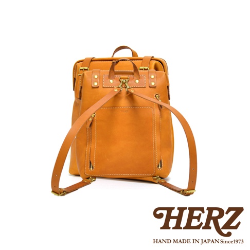 職人手作皮革後背包 R-143 加厚版，採用天然皮革製成，顏色為溫暖的棕褐色。包款設計簡潔，具有一個方形前袋，袋口及側邊有拉鍊，肩帶可調節，並配有金屬扣環，展現精緻工藝。