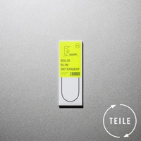 白色包裝盒頂部貼有螢光黃色標籤，印有黑色線條畫的廚房水龍頭和肥皂盤，下方標示「SOLID SLIM DETERGENT」。包裝盒下方有黑色U形輪廓。右下角有白色圓形標誌，內有箭頭和「TEILE」字樣。