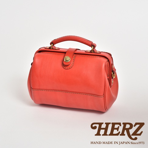 一個亮橘色的皮革口金醫生包，帶有手提把和金色五金配件，包身縫線清晰，風格復古。