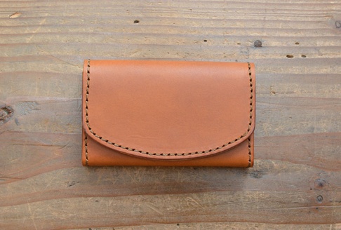 棕色皮革名片夾，以手工縫線裝飾，置於木紋背景上。