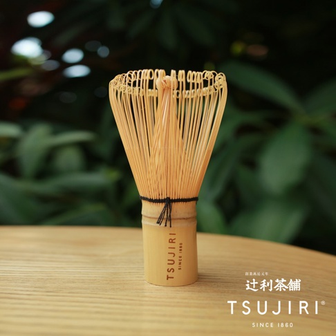 天然竹製抹茶茶刷，擁有細長的黃色竹籤，頂端呈圓形彎曲，底部有黑色細繩綁紮，竹製手柄上印有「TSUJIRI SINCE 1860」字樣。