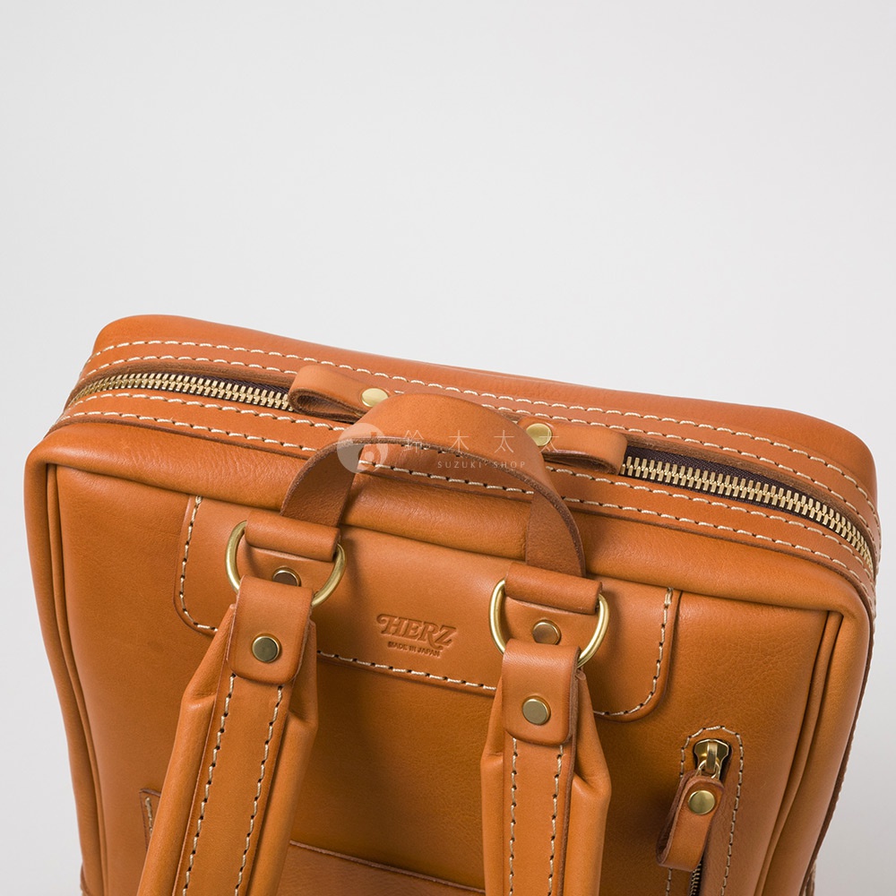 棕色皮革製成的商務後背包，帶有縫線細節、黃銅色拉鍊與金屬環。背包頂部設有提把，兩側有可調節的皮革肩帶。