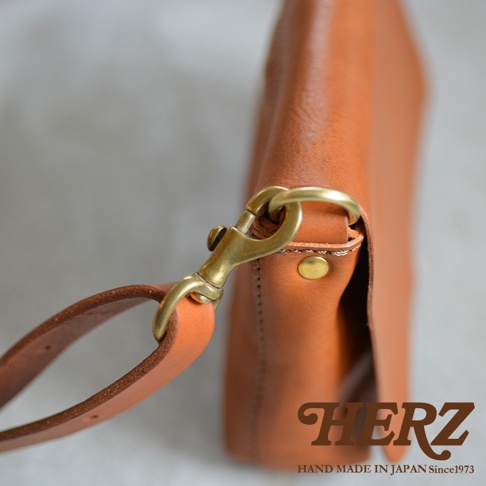 HERZ 職人手作皮革隨身斜背包，細節展示，包含黃銅色鉤扣和皮革背帶。